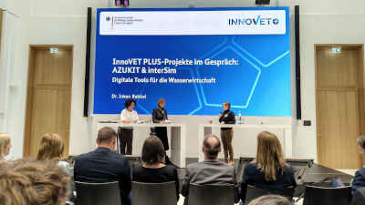 Bühne mit Leinwand mit Präsentation im Hintergrund, davor Publikum. Bundesministerin Karin Prien (Mitte) auf der Bühne im Gespräch mit Dr. Inken Rabbel (DWA, rechts) über digitale Werkzeuge für die Ausbildung in der Wasserwirtschaft. Links: Moderatorin Dr. Julia Kropf